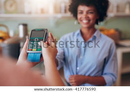 Female customer paying by credit card at juice bar. Focus on woman hands entering security pin in credit card reader.