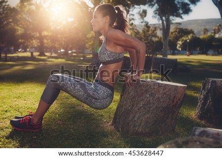 Young woman practicing push ups in a park. Side view shot of muscular female exercising with a log.