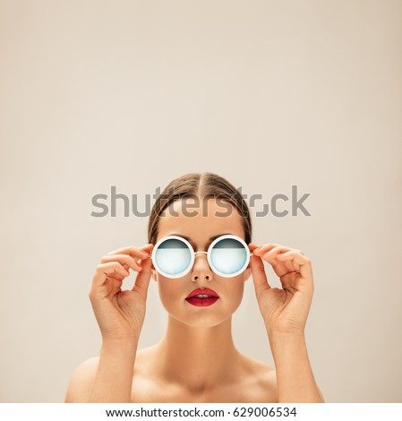 Square portrait of young woman with sunglasses against beige background. Caucasian female fashion model posing with glasses.