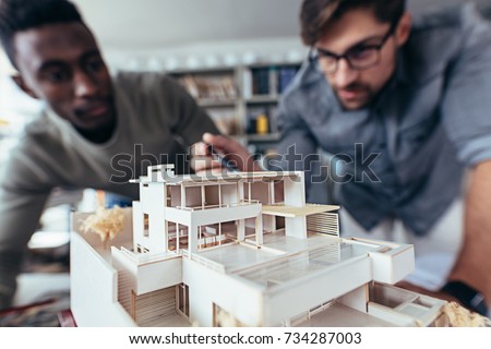 Close up shot of scale model house on table with architects. Two architects making architectural model in office together.