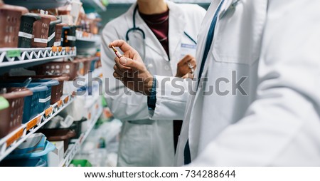 Two pharmacist looking for critical medicinal drug. Male doctor holding a medicine with female standing by in pharmacy.
