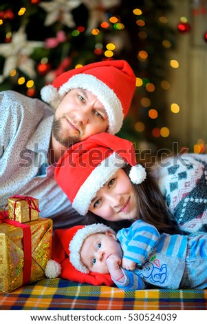 Happy family with the newborn son in santa clauss caps lie on a floor near Happy family with the newborn son in santa clauss caps lie on a floor near