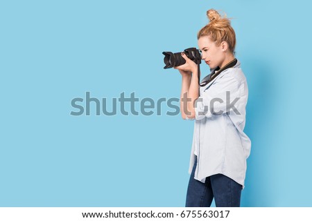 Young blonde photographer is taking a photo. Model isolated on a blue background with copy space
