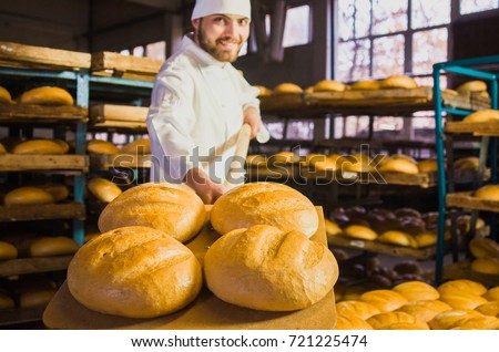 Baker. A young handsome bakery worker on the background of bread, takes bread from a stove with a wooden shovel. Industrial production of bakery products. a man in the baker's special clothing. Bakery