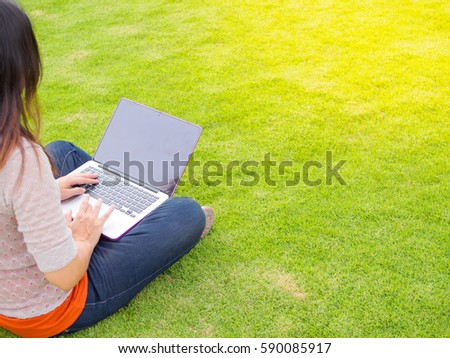 Pretty Young woman using laptop computer. Female working on laptop in an outdoor green grass field