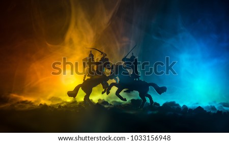 Medieval battle scene with cavalry and infantry. Silhouettes of figures as separate objects, fight between warriors on dark toned foggy background. Night scene. Selective focus