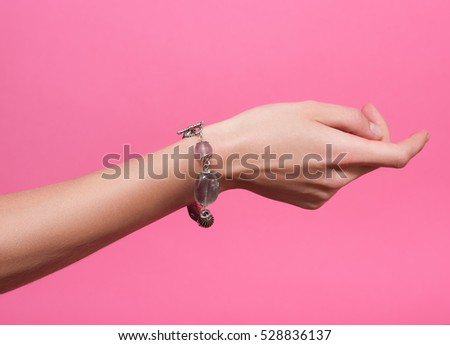 Closeup female hand with a bracelet on your wrist. Handmade jewelry and accessories. Isolated on pink background