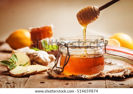 Honey in jar with honey dipper, ginger and lemon on wooden background
