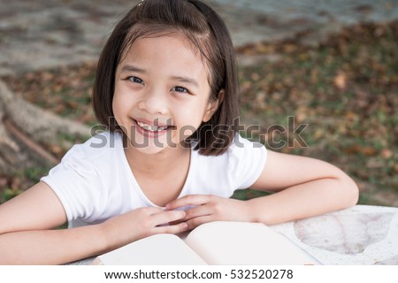 Happy Little Asian child reading a book outdoor