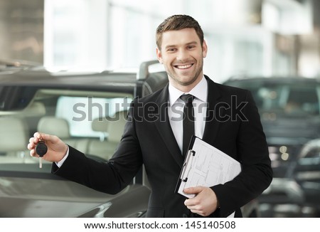 Great choise! Handsome young classic car salesman standing at the dealership holding a key