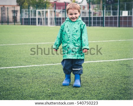 Cute funny little kid playing on the playground in a beautiful green cloak with dinosaurs. Sport, bad weather, rain.