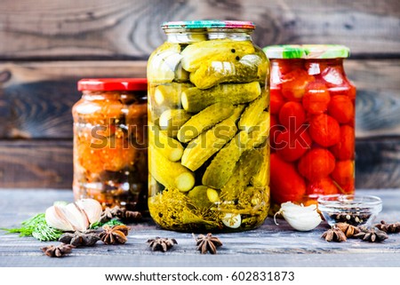 Jars of pickled vegetables: cucumbers, tomatoes, eggplants on rustic wooden background. Marinated and canned food.   