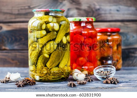 Jars of pickled vegetables: cucumbers, tomatoes, eggplants on rustic wooden background. Marinated and canned food.   