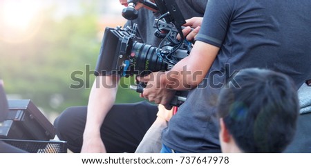 Blurry image of movie shooting or video production and film crew team with camera equipment at outdoor location and light flare effect.