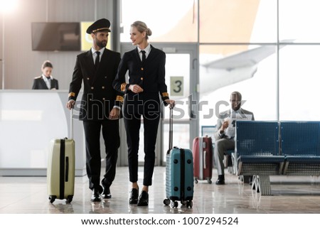 male and female pilots walking by airport lobby with suitcases
