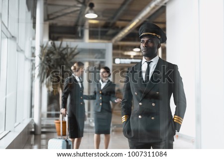 thoughtful young pilot in airport with stewardesses before flight