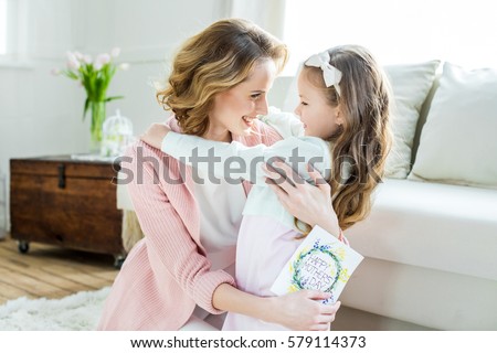 Happy mother hugging her adorable little daughter and holding greeting card for Mothers Day