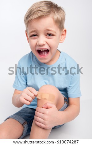stock-photo-little-boy-removing-patch-from-injured-knee-and-crying-at-camera-isolated-on-grey-610074287.jpg