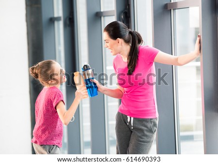 mother and daughter in pink shirts with sport bottles in gym