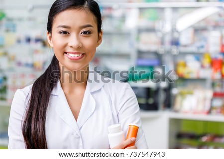 pharmacist in white coat holding containers with medication and smiling at camera