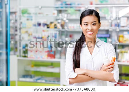 cheerful young asian pharmacist with medication smiling at camera in drugstore