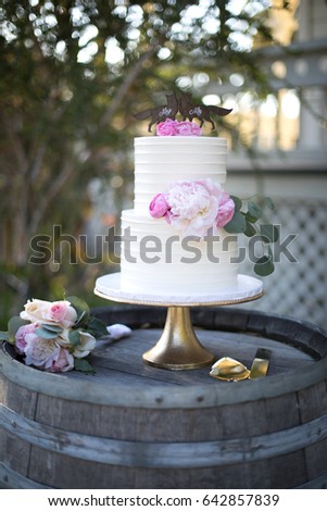 Two Tiered White Frosting Wedding Cake With Pink Flowers On Gold Stand Atop Weather Wood Wine Two Tiered White Frosting Wedding Cake With Pink Flowers On Gold Stand Atop Weather Wood Wine