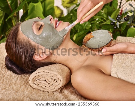 Woman with clay facial mask in beauty spa. In background tropical plants