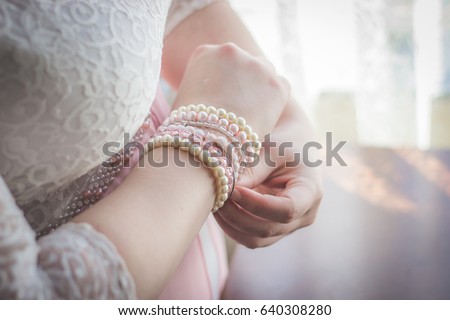 Woman putting on white and pink pearl beaded bracelets with focus on hands and wrist closeup in pink and white lace wedding dress as bridal preparation getting ready photos