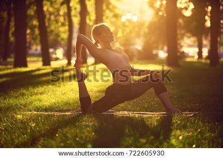 Beautiful young woman practices yoga asana King Pigeon pose rajakapotasana in the park at sunset