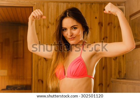 Portrait of young woman relaxing in wooden finnish sauna showing off muscles. Attractive girl in bikini resting. Spa wellbeing pleasure.