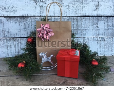 Red gift box and paper gift bag with greenery and ornaments against a white washed wall