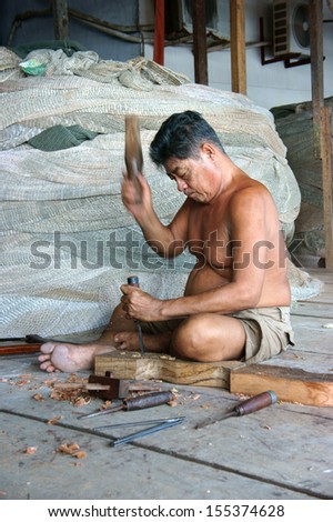 CA MAU. VIET NAM- JUNE 29. Portrait of the man with carpentry tool bore a hole in section of a tree trunk, there are some fishing net roll to fisherman catch fish. In vertical frame. June 29, 2013