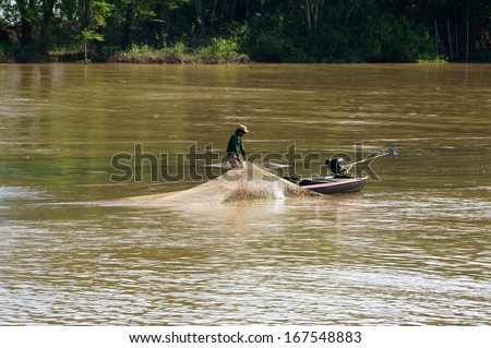 DONG THAP, VIET NAM- NOV 12: Fisherman stand on boat and do fishing on river, he spread a net to catch fish, then pull the net and beat it to reject trash in Dong Thap, Viet Nam on Nov 12, 2013