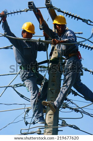 DONG THAP, VIET NAM- SEPT 23: Two Asian electrician climb high in pole to work, lineman with cable network, man repair electric post with belt safety, this is industry service, Vietnam, Sept 23, 2014
