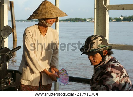 DONG THAP, VIET NAM- SEPT 19: Asian lottery ticket vendor offer Vietnamese man, many poor people earn living by raffle ticket, senior woman work on ferry boat, Vietnam, Sept 19, 2014