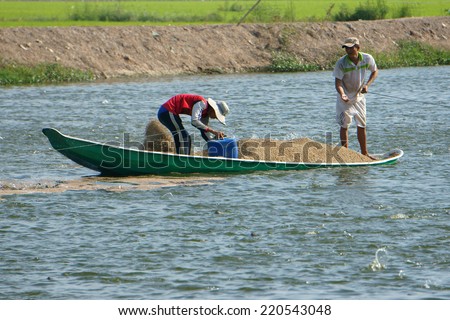 DONG THAP, VIET NAM- SEPT 23: Two Asian farmer work on lake, Vietnamese man feeding, Mekong Delta has many fish pond for fishery, heap of feed on boat, people spread on water, Vietnam, Sept 23, 3014