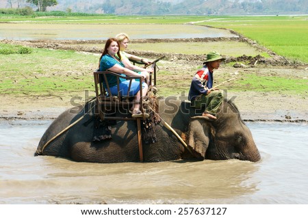 BUON ME THUOT, VIET NAM- FEB 25: Group of tourist traveling Vietnamese countryside, traveler ride elephant, cross rural with green flield, this is Daklak's travel product, Vietnam, Feb 25, 2015