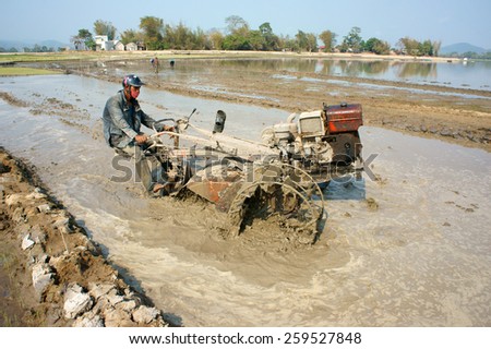 DAK LAK, VIET NAM- FEB 25: Asian farmer working on rice field, Vietnamese man plough paddy plantation for new crop by tractor, repair soil for sow rice in hot day, Daklak, Vietnam, Feb 25, 2015