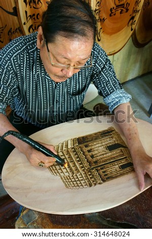 QUY NHON, VIET NAM- AUG 23: Vietnamese artist doing wood engraving by fire pen, man engrave Han Mac Tu poem at souveir shop of Genh Rang tourist area, a famous poet, Quynhon, Vietnam, Aug 23, 2015