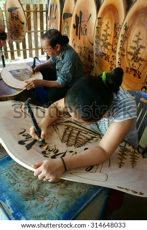 QUY NHON, VIET NAM- AUG 23: Vietnamese artist doing wood engraving by fire pen, man engrave Han Mac Tu poem at souveir shop of Genh Rang tourist area, a famous poet, Quynhon, Vietnam, Aug 23, 2015