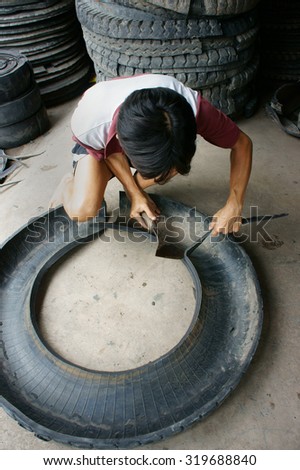 VINH LONG, VIET NAM- JULY 27: Vietnamese worker working at Mekong Delta trade village to recycle tire, man cut out rubber from tyre, Vinhlong, Vietnam, July 27, 2015