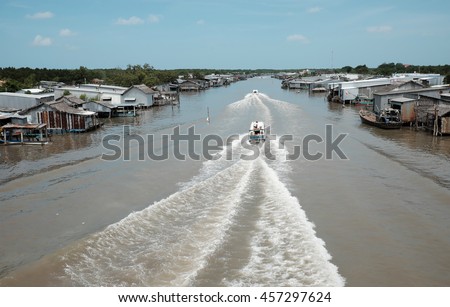 Lively scene on waterway at Mekong Delta, Vietnam. Motor boat move in fast on Ca Mau river, motorboat make wave on water, riverside residential with house make from metal sheet at Camau, Vietnam