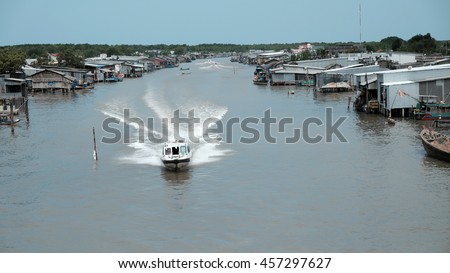 Lively scene on waterway at Mekong Delta, Vietnam. Motor boat move in fast on Ca Mau river, motorboat make wave on water, riverside residential with house make from metal sheet at Camau, Vietnam