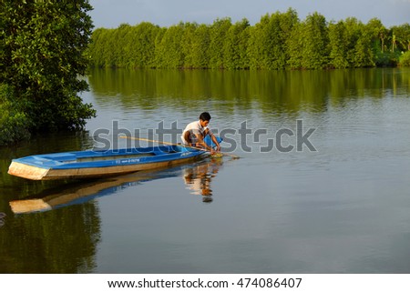 CA MAU, VIET NAM- JULY 16, 2016: Vietnamese man catch fish on river, people and row boat reflect on water, beautiful green tree from mangrove forest make wonderful scene in evening at Mekong Delta