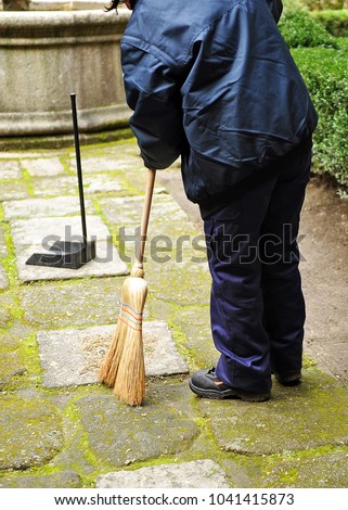 Sweeper, municipal cleaning worker sweeping autumn leaves in the garden