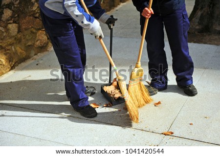 Two sweepers, municipal cleaning workers sweeping autumn leaves on town sidewalk