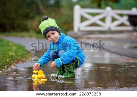 Little boy, jumping in muddy puddles in the park, rubber ducks in the puddle