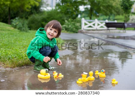 Little boy, jumping and playing in muddy puddles in the park, rubber ducks in the puddle