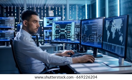 System Security Specialist Working at System Control Center. Room is Full of Screens Displaying Various Information.