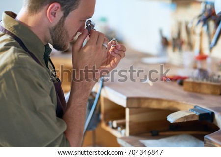 Side view portrait of jeweler inspecting diamond ring through magnifying glass in workshop